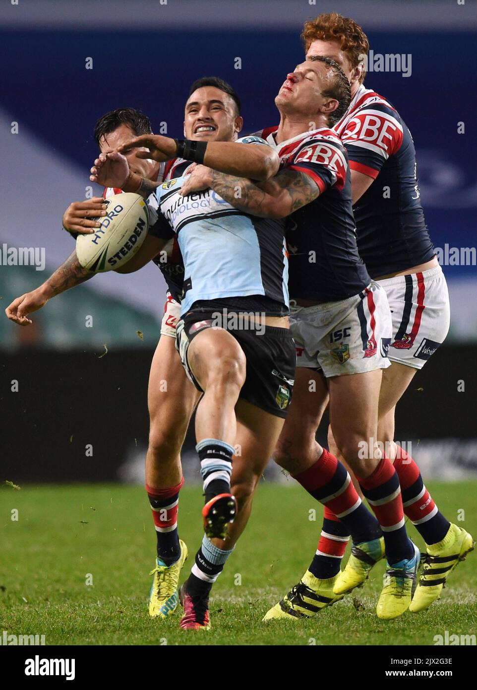 Valentine Holmes (Mitte) der Sharks wird am Montag, den 18. Juli 2016, im NRL-Spiel der Runde 19 zwischen den Sydney Roosters und den Cronulla Sutherland Sharks im Allianz Stadium in Sydney von Jake Friend (rechts) und Mitchell Pearce (links) der Roosters angegangen. (AAP-Bild/Paul Miller) Stockfoto