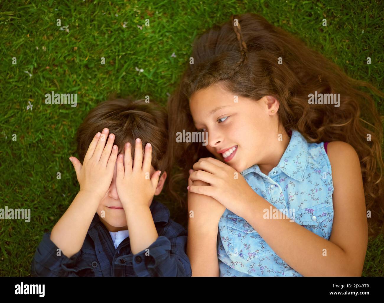 Brüder und Schwestern bilden die besten Spielkameraden. High-Angle-Aufnahme eines Jungen, der mit seiner Schwester draußen auf dem Rasen Peekaboo spielt. Stockfoto