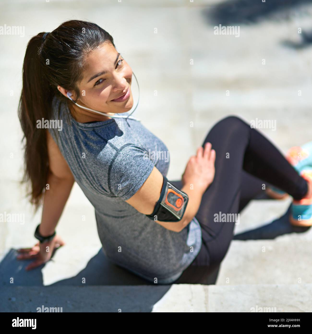 Ihre Fitness verbessert sich stetig. Eine sportliche junge Frau hört Musik, während sie draußen sitzt. Stockfoto