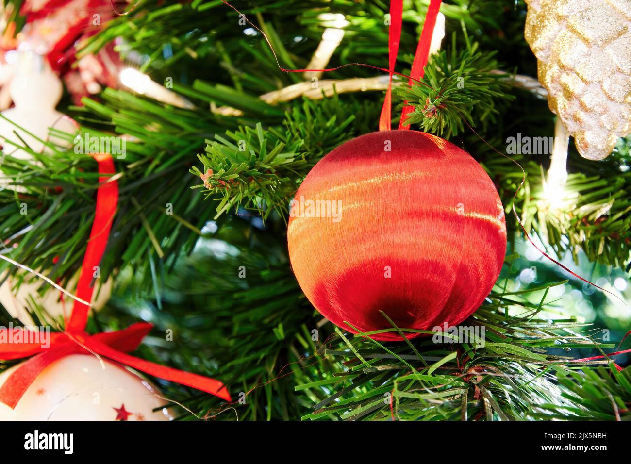 Rot glänzende Weihnachtskugel auf dem grünen Baumzweig. Hintergründe zum neuen Jahr Stockfoto