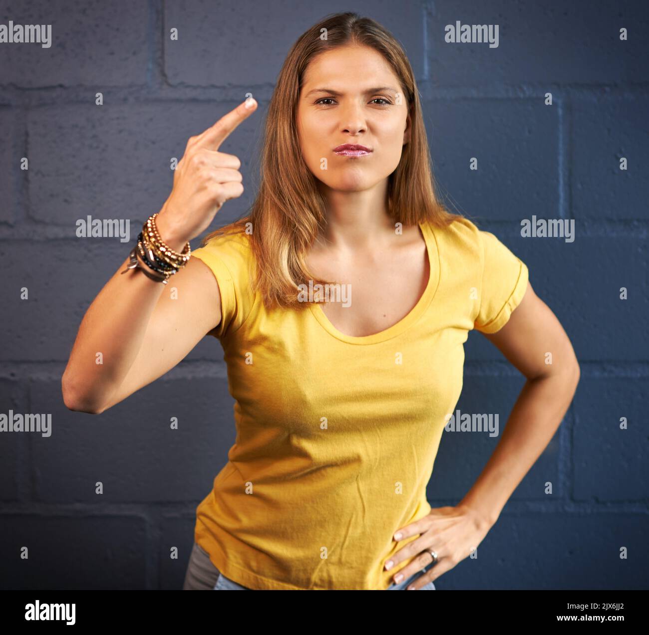 Nicht cool. Beschnittenes Porträt einer jungen Frau, die wütend auf einen Backsteinwand-Hintergrund schaut. Stockfoto
