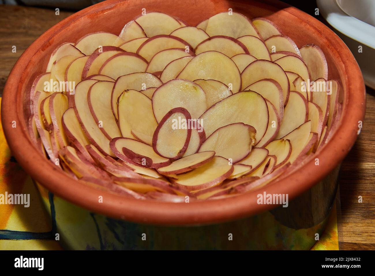 Kartoffelgratin in einer blumenförmigen Keramikschale ist bereit zum Backen im Ofen Stockfoto