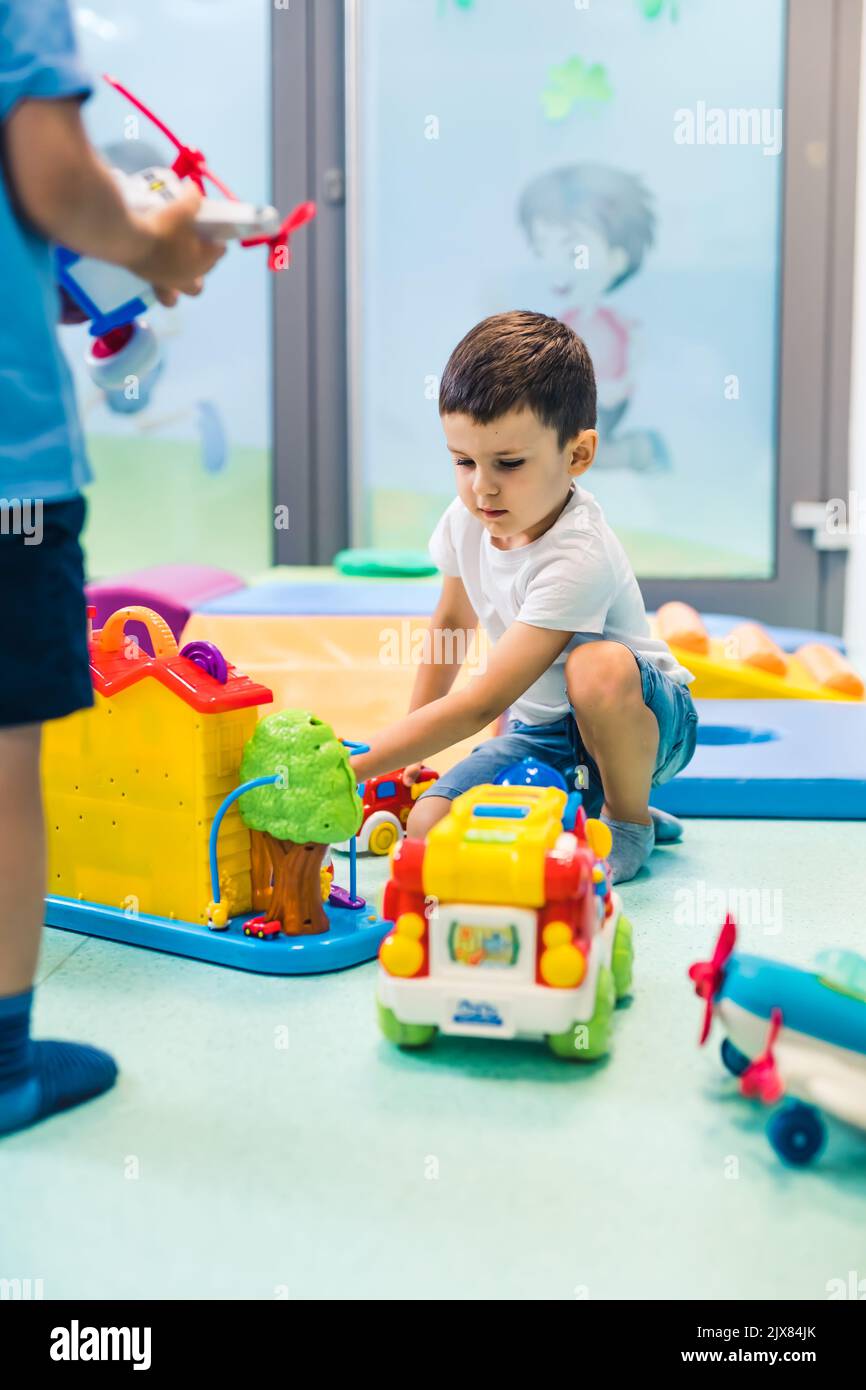 Vorstellungskraft und kreative Denkentwicklung. Sprach- und Sozialkompetenz. Kleinkind spielt mit bunten Plastikspielzeug und bunten Auto in einem Kindergarten Spielzimmer. Hochwertige Fotos Stockfoto