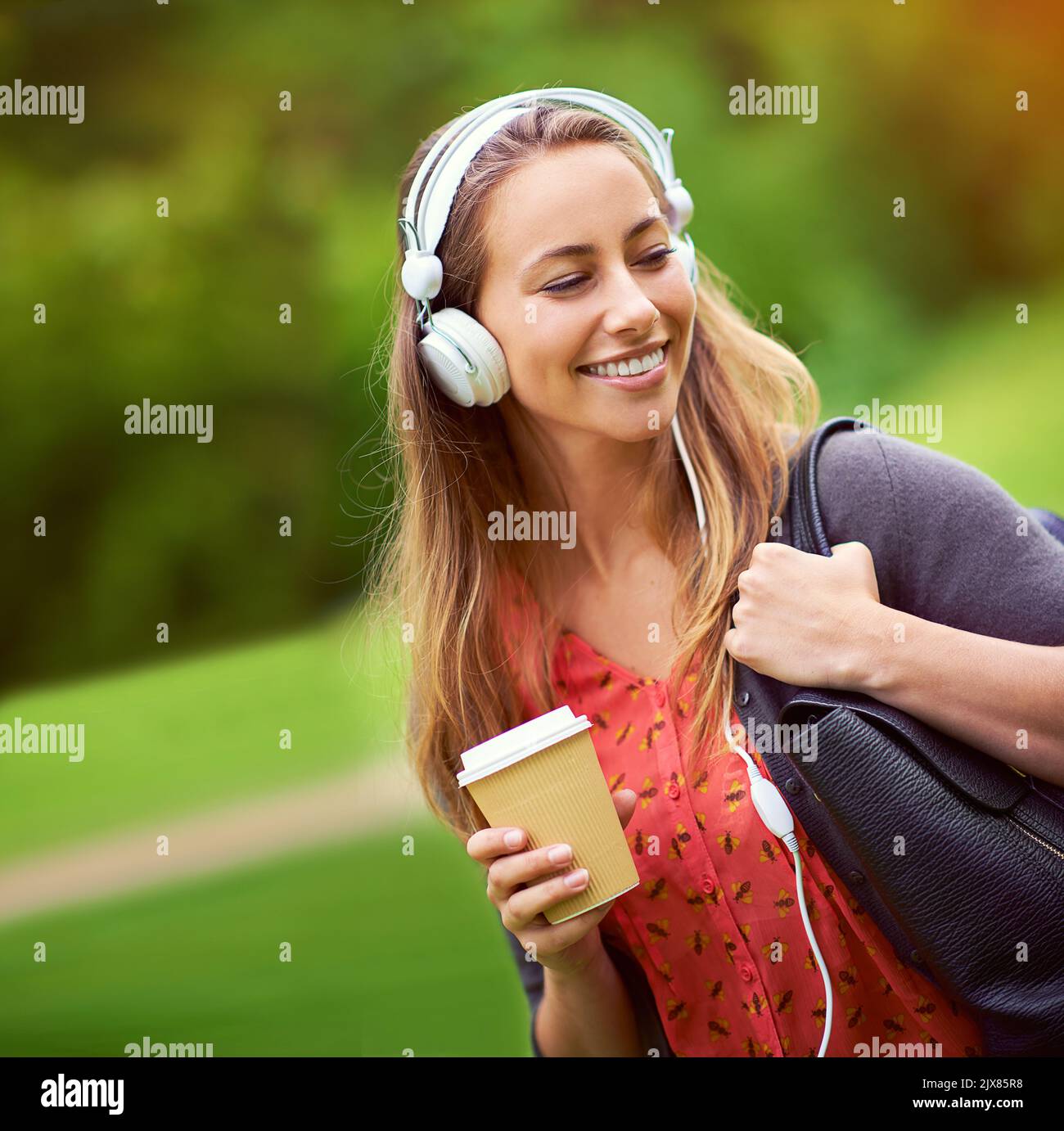 Ein Spaziergang durch den Park mit ihrem Kaffee und ihrer Musik. Eine junge Frau, die Musik hört, während sie unterwegs einen Kaffee trinken. Stockfoto