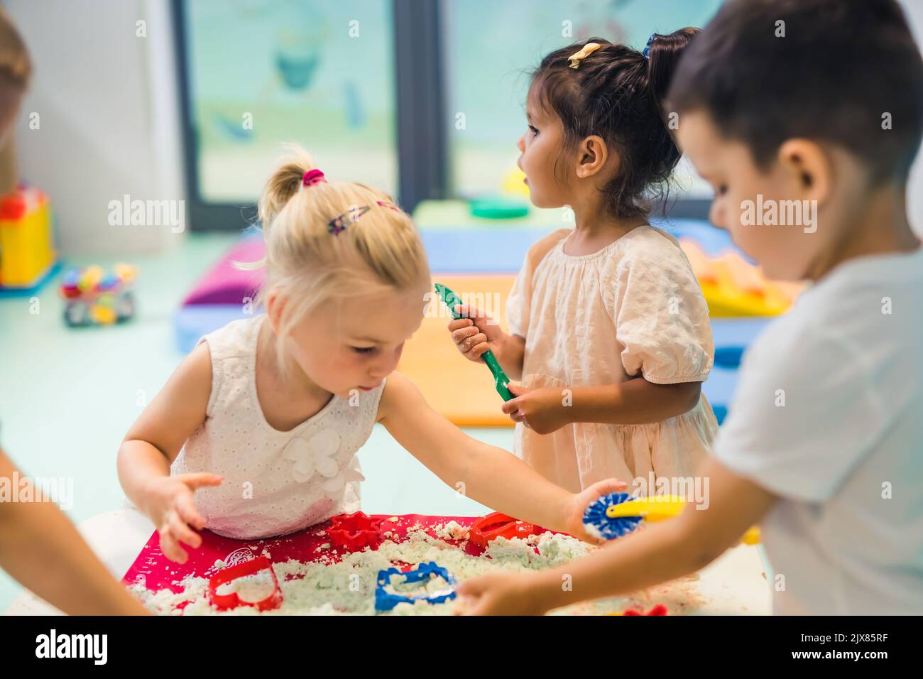 Lustiges sensorisches Spiel mit formbarem kinetischem Sand im Kindergarten. Kleinkinder stehen um den Tisch herum und verwenden verschiedene Werkzeuge zum Formen von Sand wie bunte und strukturierte Rollnadeln, Schneider, Silikonhüllen. Feinmotorik und kreative Entwicklung . Hochwertige Fotos Stockfoto