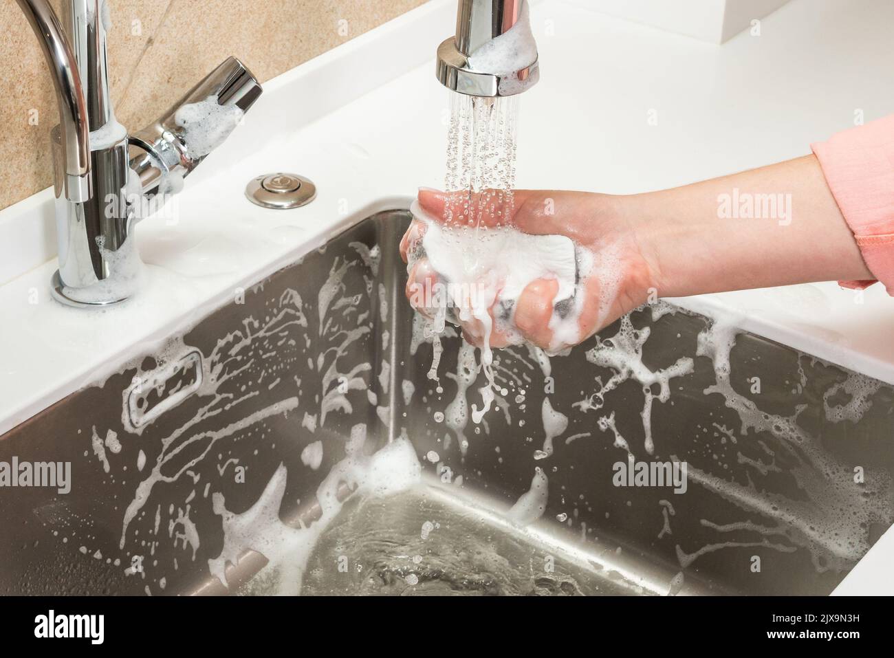 Schwamm in der Hand einer Frau wird mit Leitungswasser abgewaschen Stockfoto