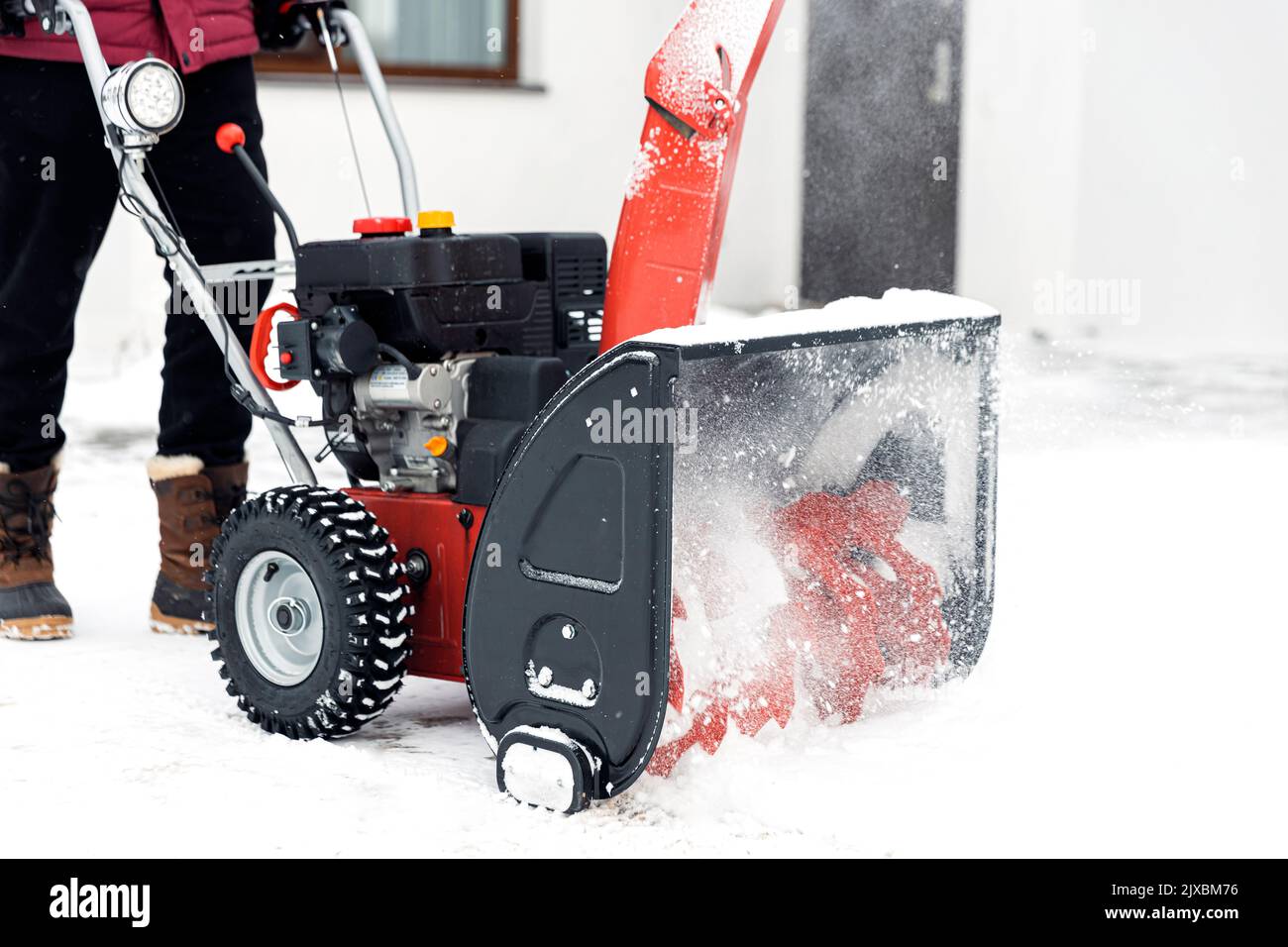 Nahaufnahme des roten Schneefräsers in Aktion. Älterer älterer Mann im Freien vor dem Haus, der Schneefräsmaschine zum Entfernen von Schnee auf dem Hof verwendet. Schneefräse im Winter vor dem Haus. Junger Arbeiter, der Schnee bläst Stockfoto