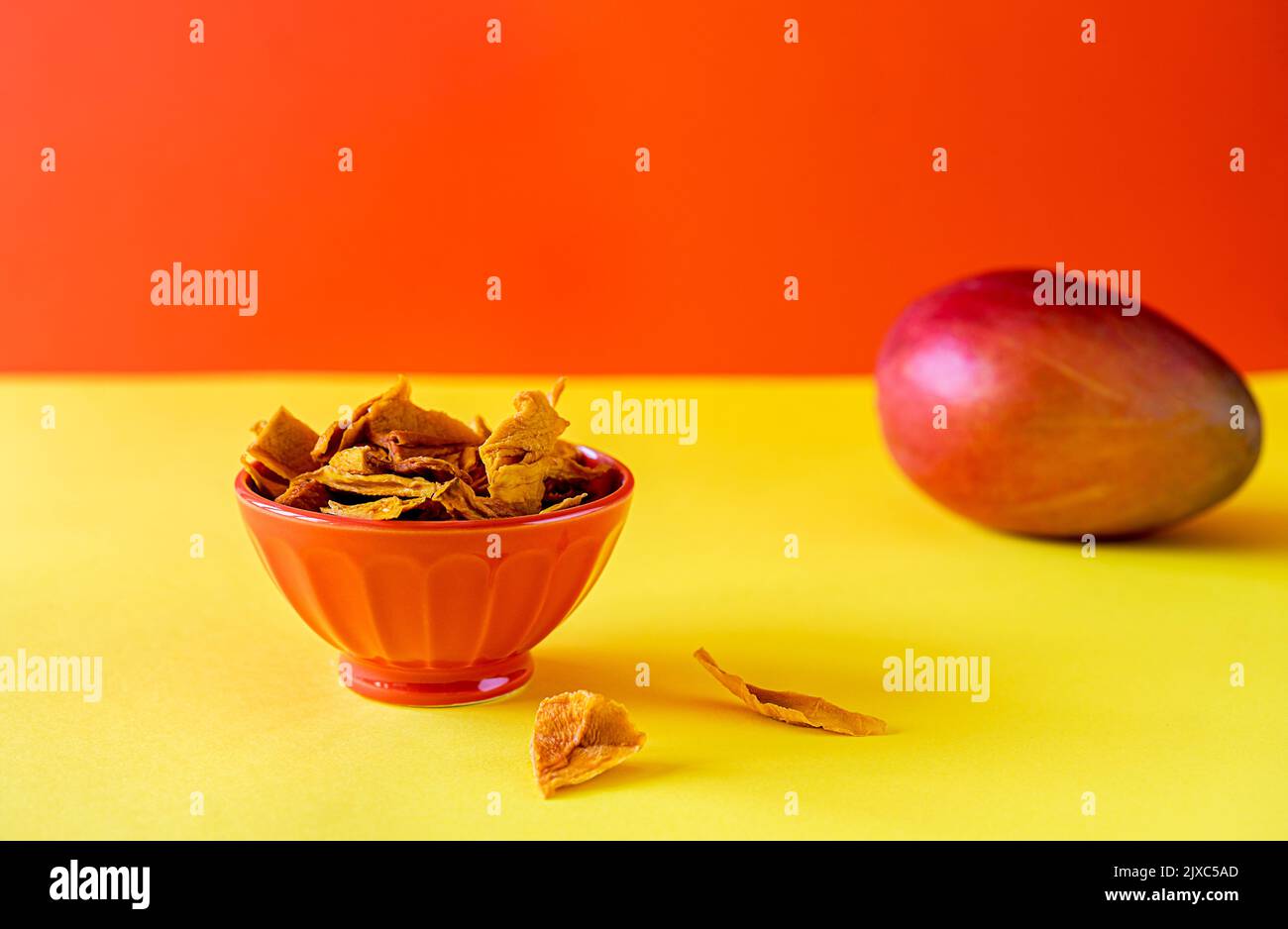 Mangochips in der Schüssel auf gelbem und orangefarbenem Hintergrund Stockfoto
