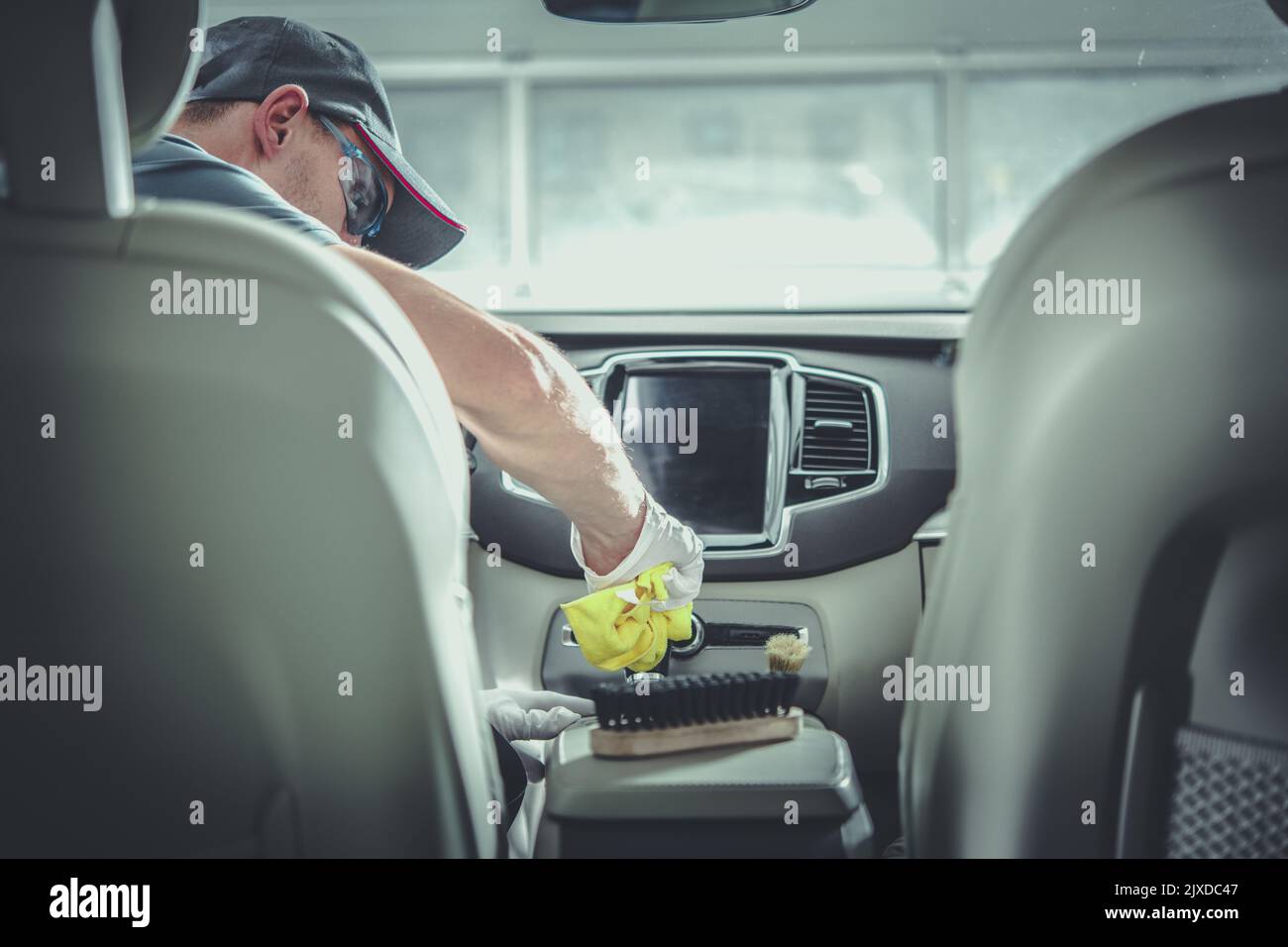 Rückansicht Foto von Auto Detailing Service Worker sitzen auf dem Fahrer Ledersitz präzise Reinigung jedes Element des Fahrzeuginnenraumteils mit dem Stockfoto