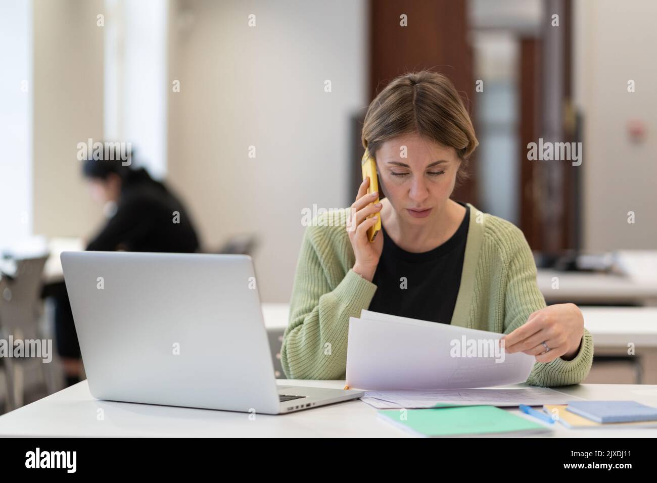 Frau mittleren Alters, die mit Dokumenten beschäftigt ist, die auf dem Mobiltelefon sprechen und auf dem Campus arbeiten. Bildung. Stockfoto