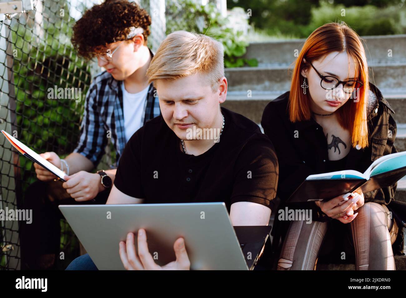 Drei junge, konzentrierte, ruhige Menschen, zwei Männer und eine rothaarige Frau in einer Brille, die am Laptop arbeitete und Bücher las. Hobby Stockfoto