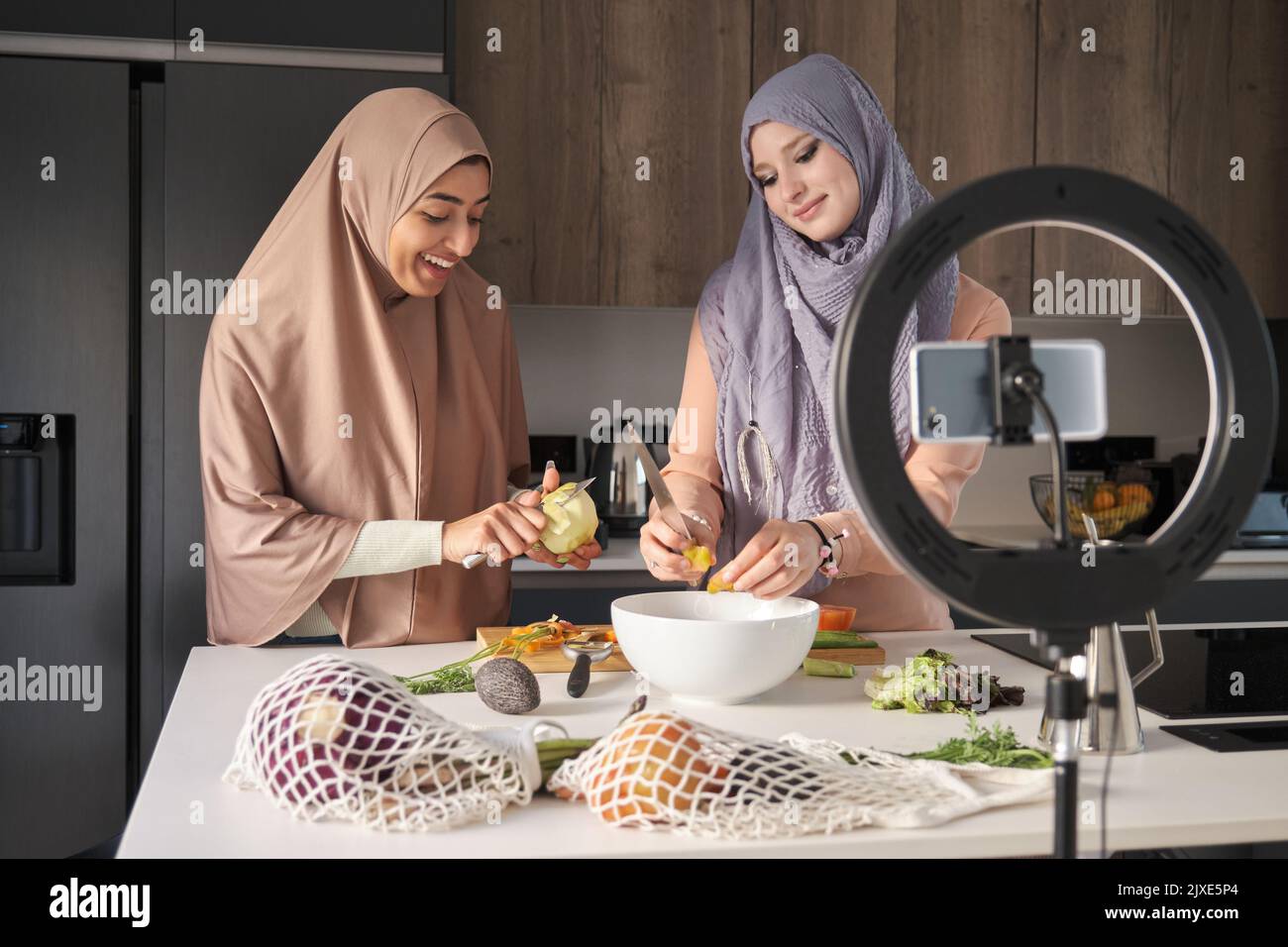 Zwei muslimische Inhaltsschöpfer schneiden, hacken und schälen Gemüse in der Küche. Stockfoto