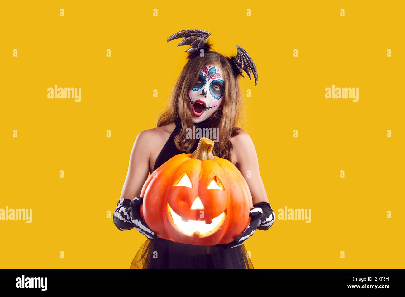 Mädchen in Halloween Kostüm hält Jack o Laterne und Blick auf die Kamera mit überraschter Ausdruck Stockfoto