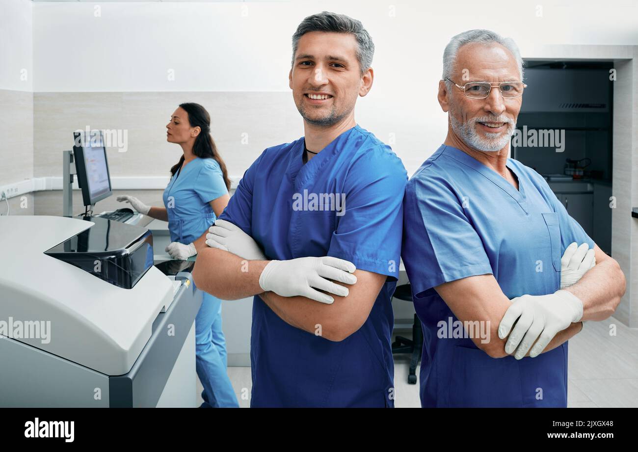 Labortechniker stehen vor dem Hintergrund eines medizinischen Labors, während eine Assistentin mit Laborgeräten arbeitet Stockfoto