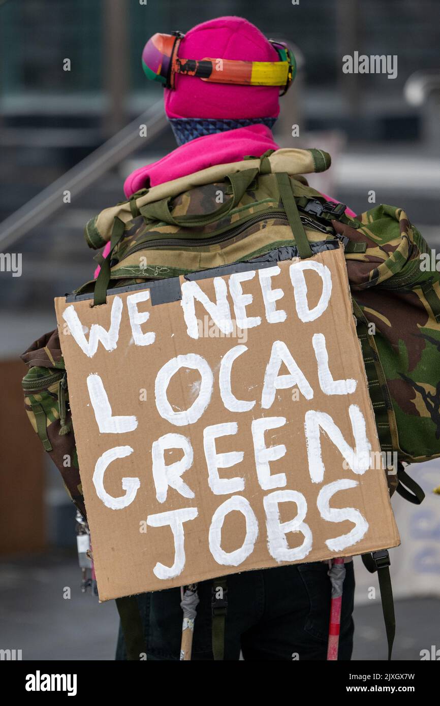 Ein Protestor trägt ein Schild mit der Aufschrift ÒWe Need local Green jobsÓ während eines Protestes im Senedd in Cardiff, Großbritannien. Stockfoto