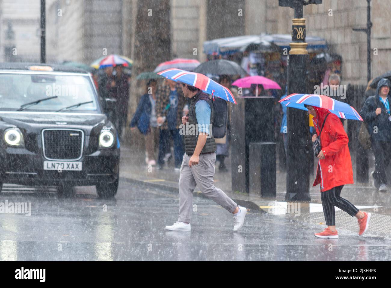 Westminster, London, Großbritannien. 7. September 2022. Heftiger Regen kam in London an. Menschen, die bei der Überquerung von Whitehall unter den Sonnenschirmen von Union Jack geschützt wurden Stockfoto