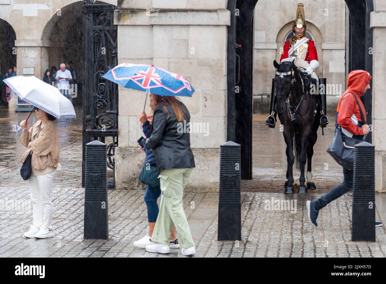 Westminster, London, Großbritannien. 7. September 2022. Heftiger Regen kam in London an. Touristen geschützt unter Sonnenschirmen in Whitehall. Berittene Soldaten in der Wache Stockfoto