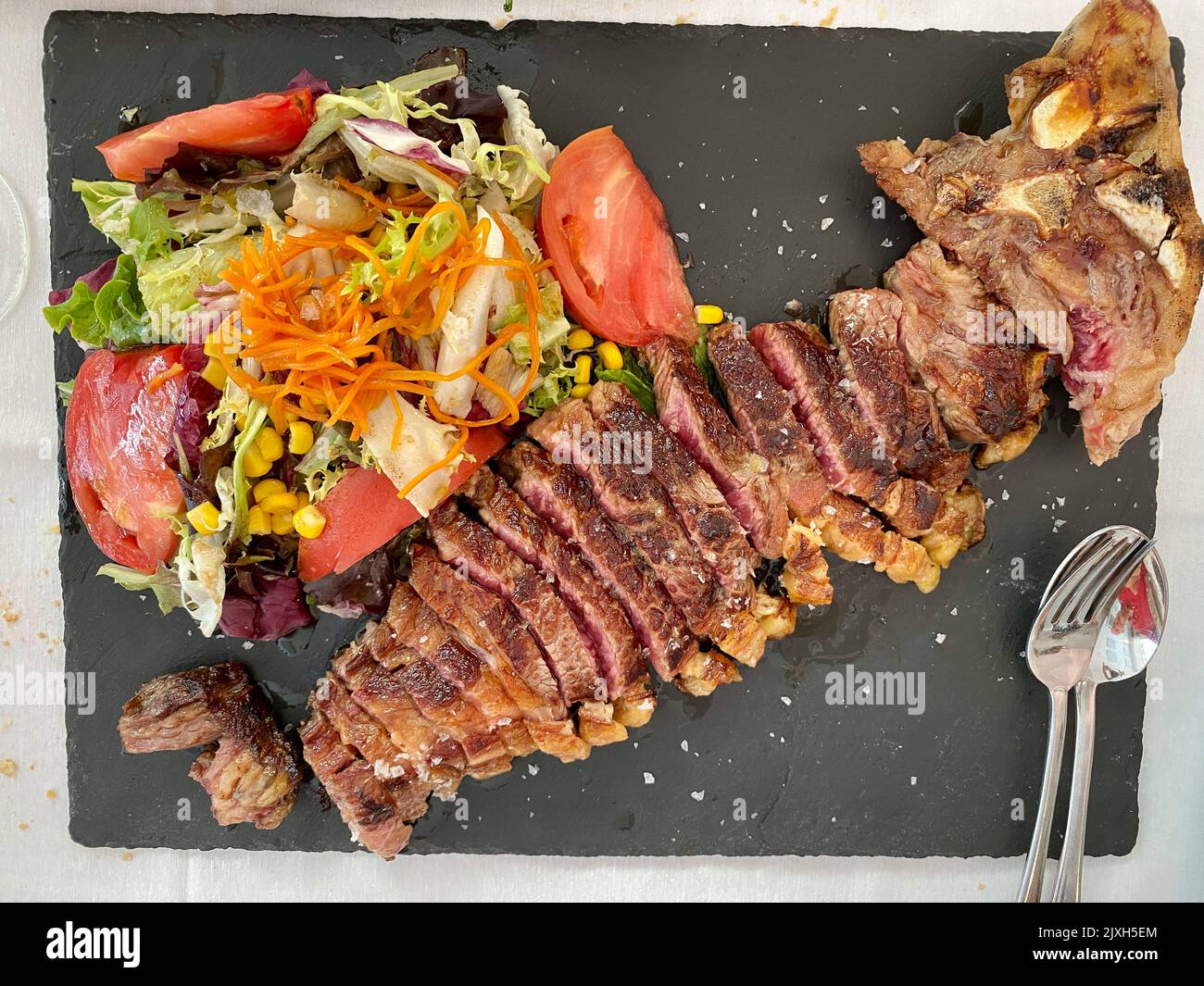 Gebackenes Kalbssteak mit Salat und Gemüse. Auf schwarzem Hintergrund. Draufsicht. Rustikaler Stil. Stockfoto