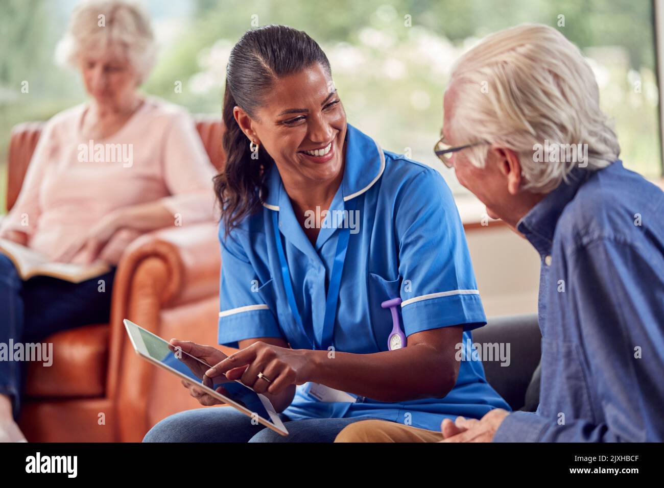 Seniorenpaar Zu Hause Mit Einem Mann, Der Mit Einer Krankenschwester Oder Einem Pflegepersonal Über Ein Digitales Tablet Spricht Stockfoto