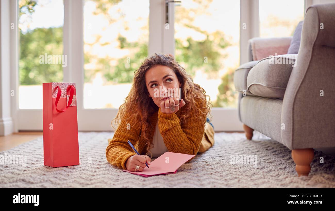 Frau In Kuscheligem Warmen Pullover, Die Zu Hause Auf Dem Boden Liegt, Schreibt Grußkarten Oder Briefe Stockfoto