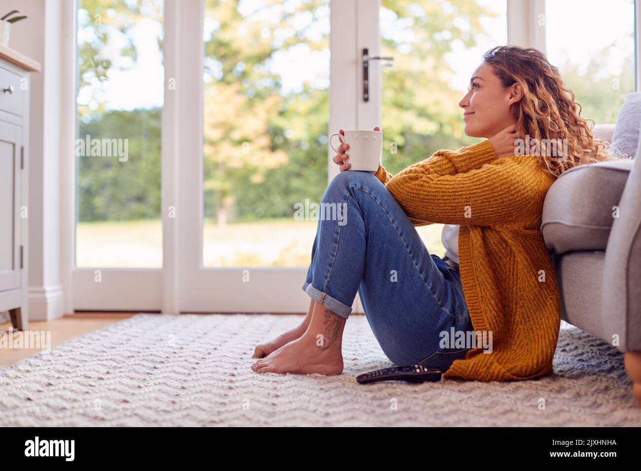 Junge Frau Im Gemütlichen Warmen Pullover Sitzt Auf Dem Boden Zu Hause Blick Aus Dem Fenster Mit Heißem Getränk Stockfoto
