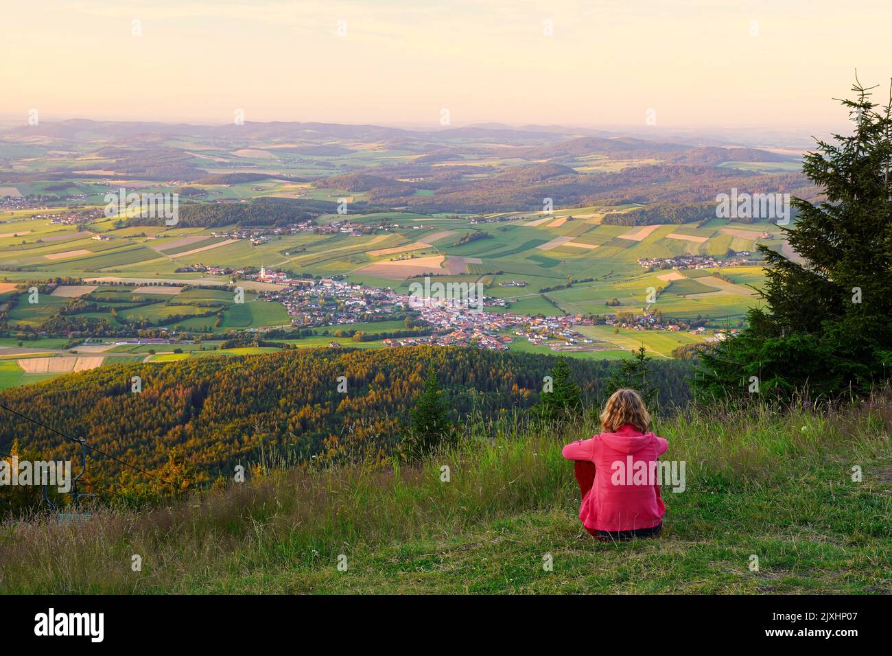 Eine kaukasische Frau, die auf dem Berg hoher Bogen sitzt und nach Neukirchen beim Heiligen Blut schaut, einer Kleinstadt im Bayerischen Wald. Lamer Winkel, Bezirk Stockfoto