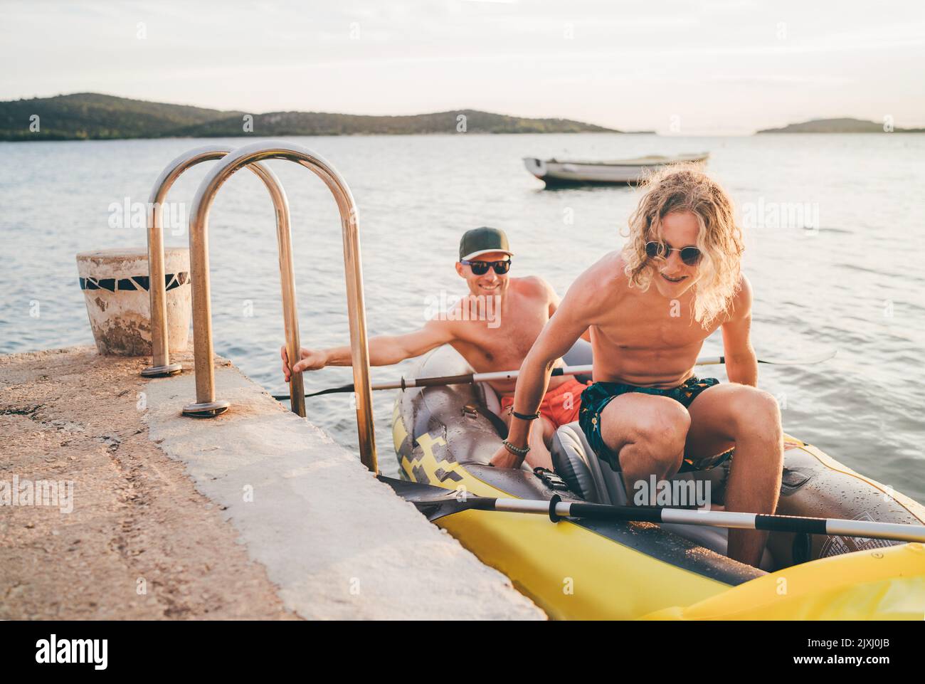 Vater mit Teenager-Sohn auf dem leuchtend gelben aufblasbaren Kajak, der von der Abendfahrt am Adriatischen Hafen in Kroatien in der Nähe von Sibeni zurückkehrt Stockfoto