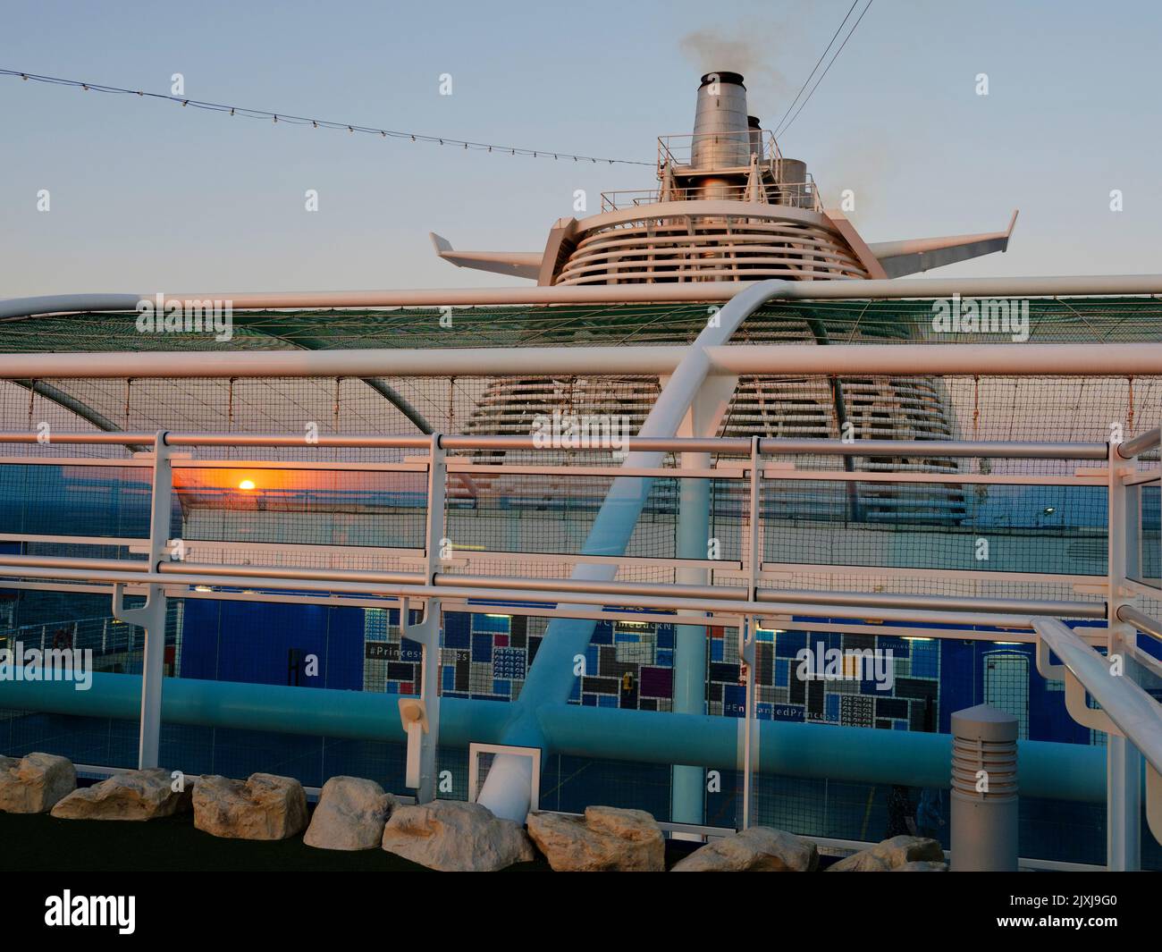 Vom obersten Deck eines Kreuzfahrtschiffs auf der Nordsee blicken wir auf die Trichter und den Überbau des Schiffes. Es ist Sonnenuntergang, und die untergehende Sonne Ref Stockfoto