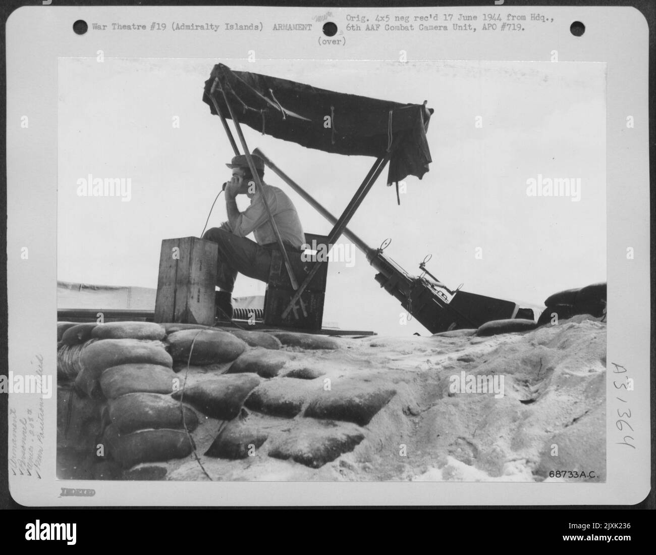 Pvt. Robert Linton aus Martinsburg, West Virginia, sitzt an der Alarmposition seiner 40-mm-Flak-Waffe der 208.-Flak-Batterie auf den Admiralty Islands. Der Sonnenschirm wurde von Pvt improvisiert. Linton, um sich vor den heißen Tropen zu schützen Stockfoto