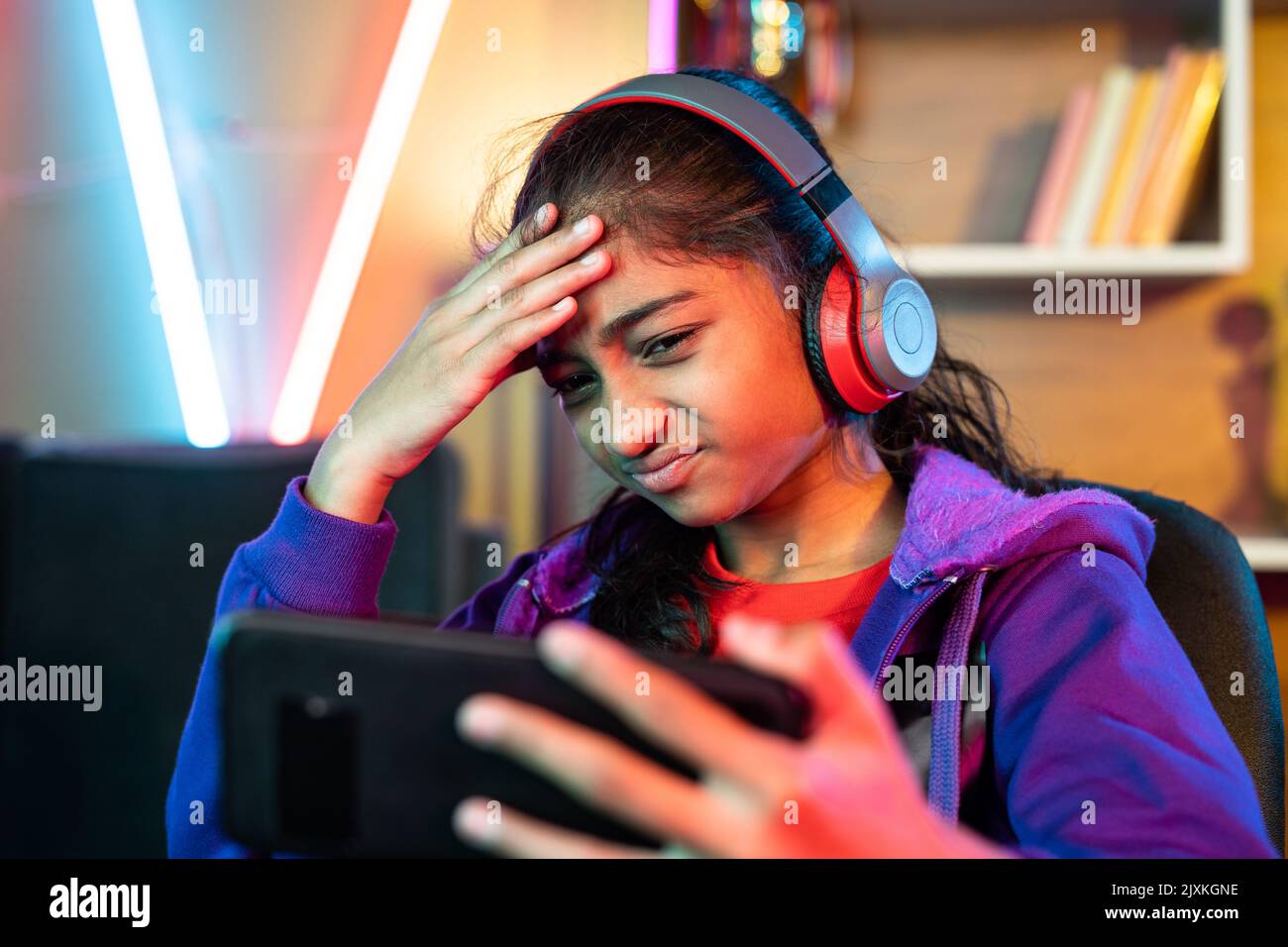 Trauriges Mädchen mit Kopfhörern verliert Spiel, während Videospiel auf Handy zu Hause spielen - Konzept der Konkurrenz, Technologie und Unterhaltung Stockfoto
