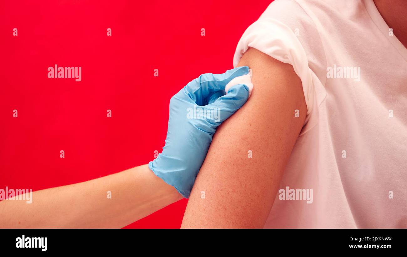 Studioaufnahme Einer Frau, Die Vor Der Injektion Oder Impfung Gegen Roten Hintergrund Den Arm Abgetupft Hat Stockfoto
