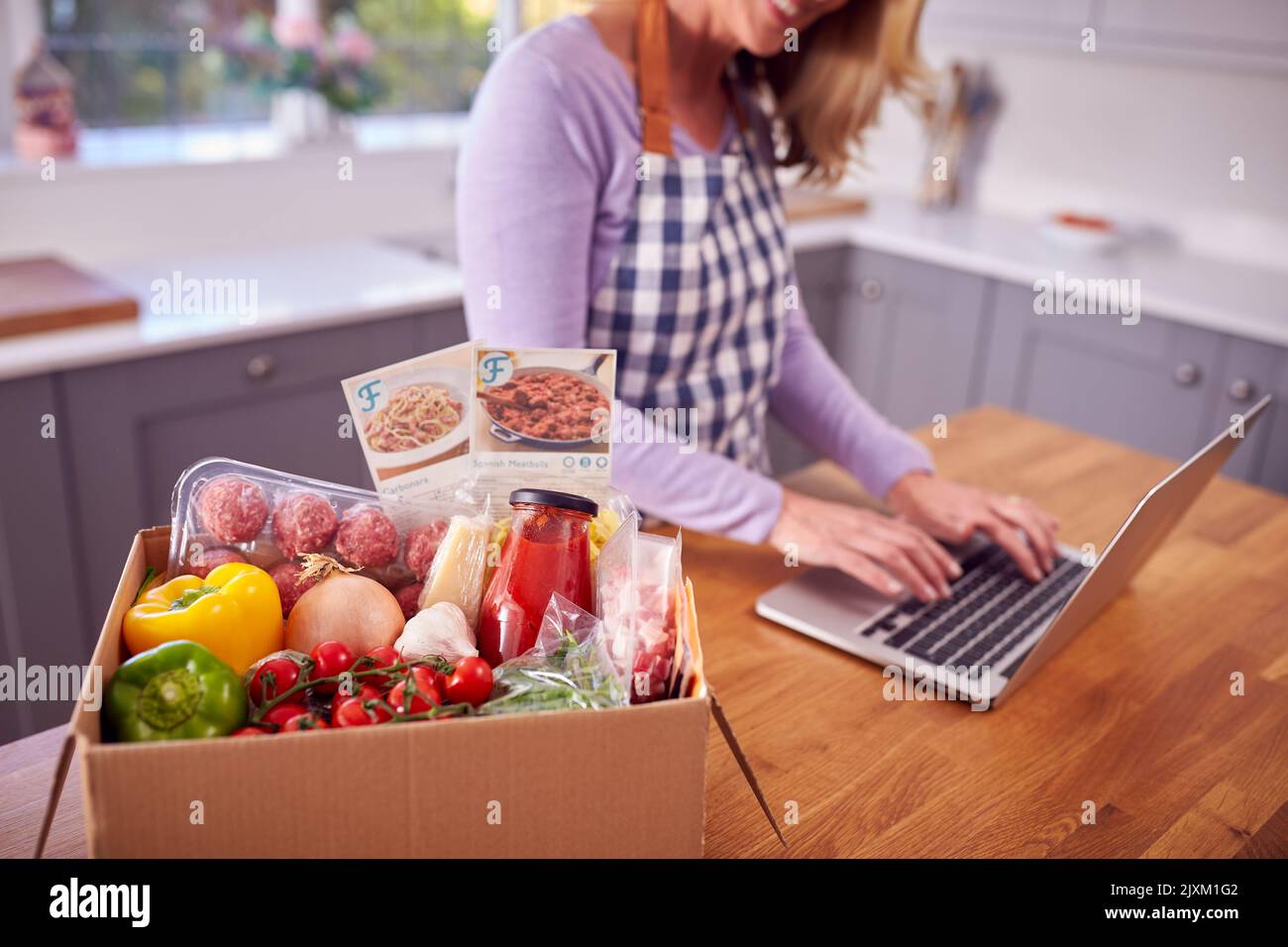 Reife Frau In Der Küche Mit Laptop Zu Finden Rezept Für Online-Mahlzeit Lebensmittel-Kit Nach Hause Geliefert Stockfoto