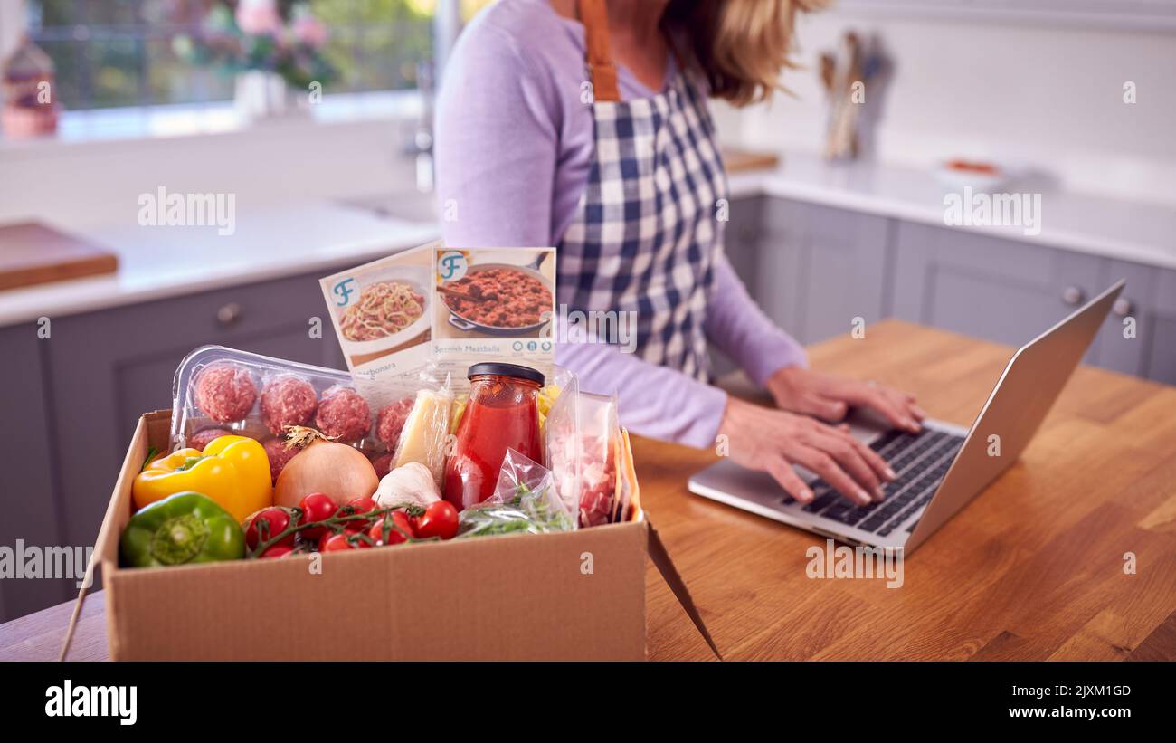 Reife Frau In Der Küche Mit Laptop Zu Finden Rezept Für Online-Mahlzeit Lebensmittel-Kit Nach Hause Geliefert Stockfoto