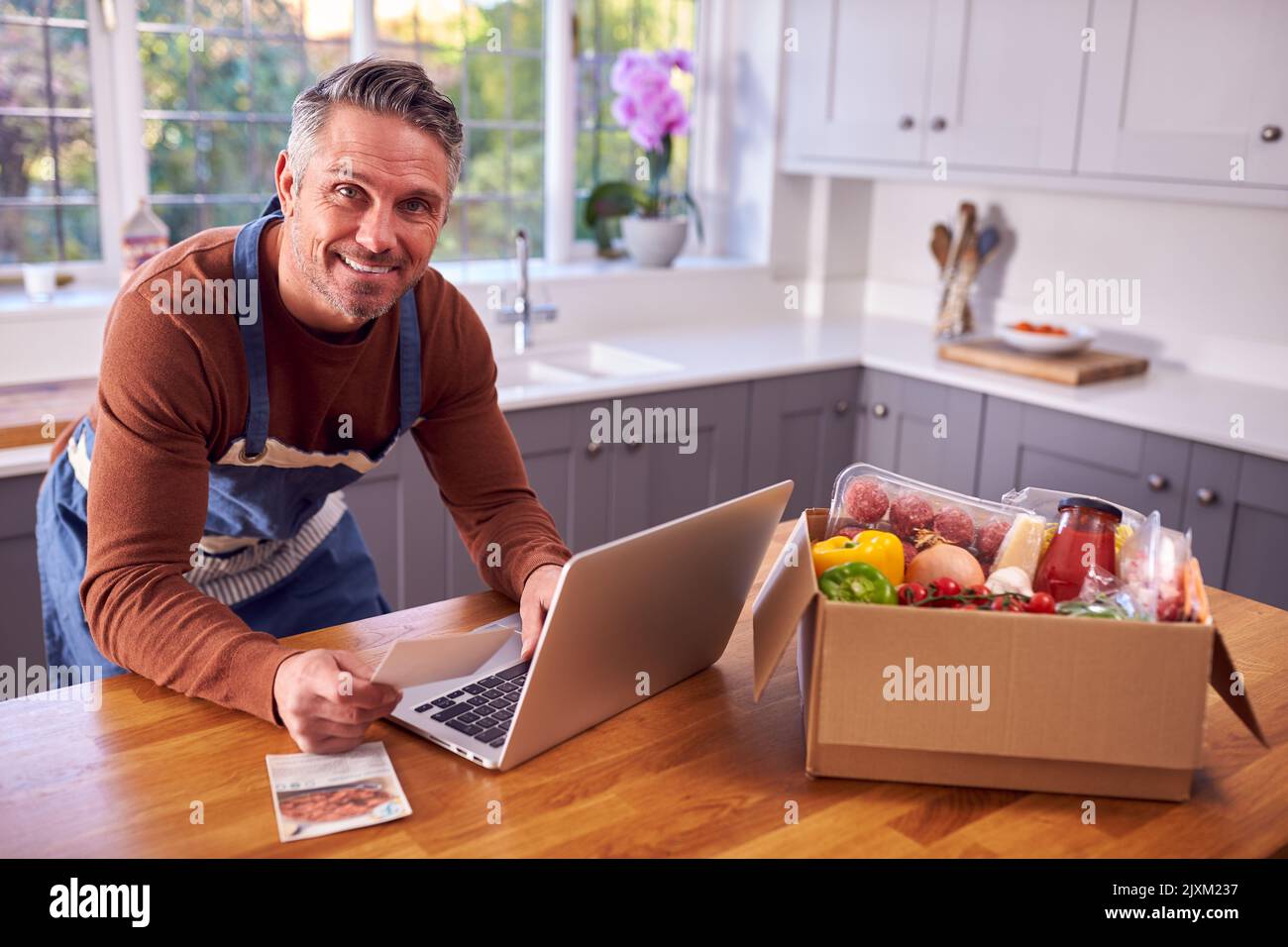 Reifer Mann In Der Küche Mit Laptop Zu Finden Rezept Für Online-Mahlzeit Lebensmittel-Kit Nach Hause Geliefert Stockfoto