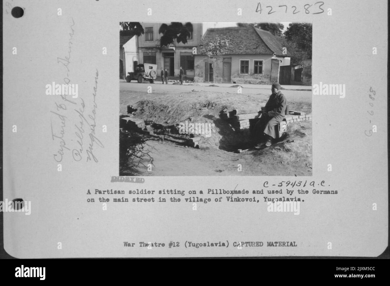 Ein Partisanensoldat, der auf einem von den Deutschen hergestellten und benutzten Pillkasten auf der Hauptstraße im Dorf Vinkovci, Jugoslawien, sitzt. Stockfoto