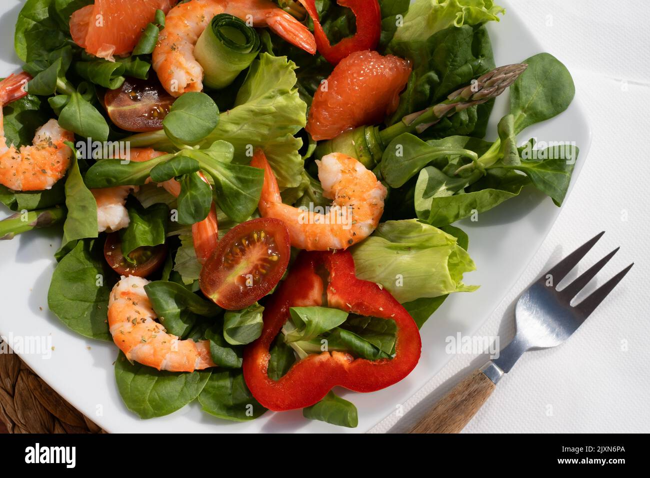 Frische Salatplatte mit Garnelen, Gurken, frischem Spargel, Tomaten und gemischtem Gemüse auf einem Holztisch. Gesunde Ernährung Stockfoto