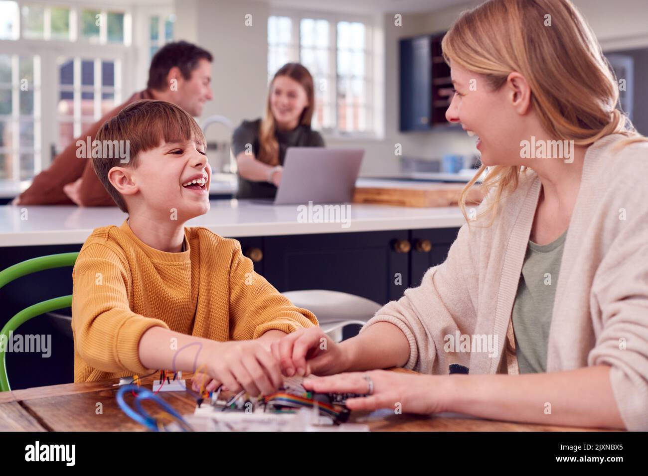 Mutter Hilft Sohn Mit Elektronik-Projekt Sitzen Am Küchentisch Zu Hause Mit Laptop Stockfoto