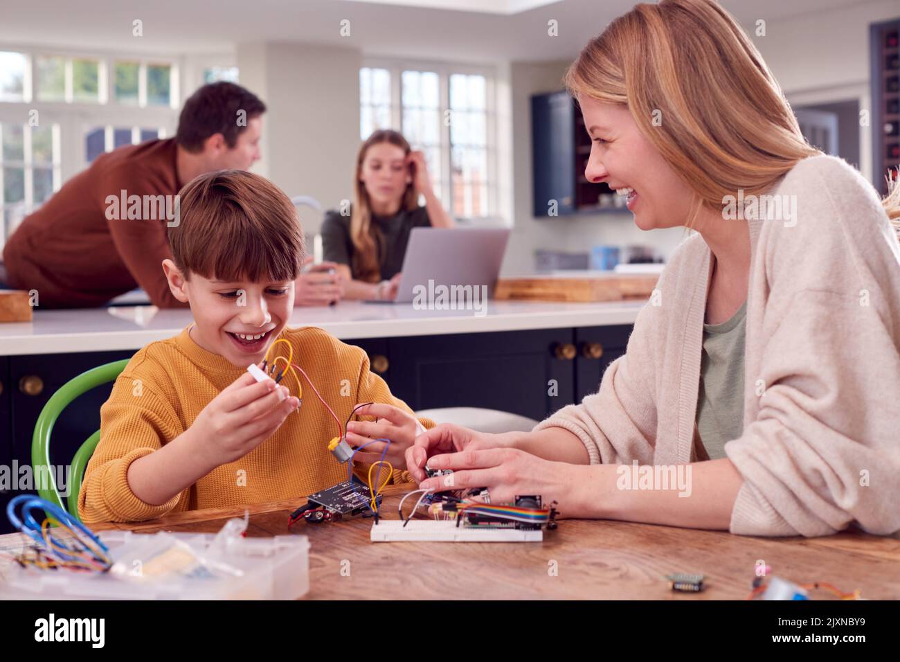 Mutter Hilft Sohn Mit Elektronik-Projekt Sitzen Am Küchentisch Zu Hause Mit Laptop Stockfoto