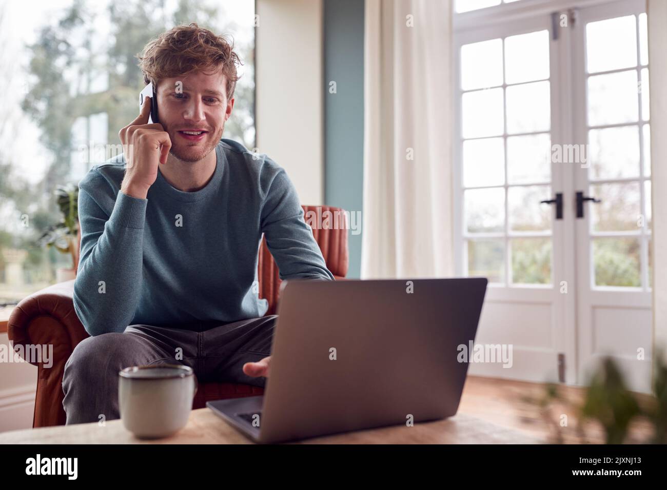 Mann, Der Von Zu Hause Aus Mit Laptop Und Mobiltelefon Arbeitet Stockfoto