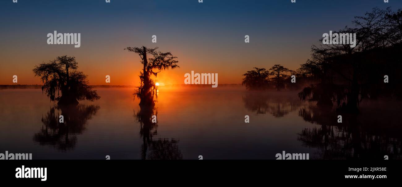 Panoramabild eines Sonnenaufgangs mit Sonnenlicht durch den Nebel am Lake Dauterive Stockfoto