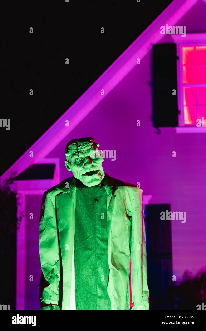 Frankenstein, ein unheimliches, lebensgroßes Monster, das grün vor einem lila beleuchteten Haus im Oktober an Haloween glühte Stockfoto