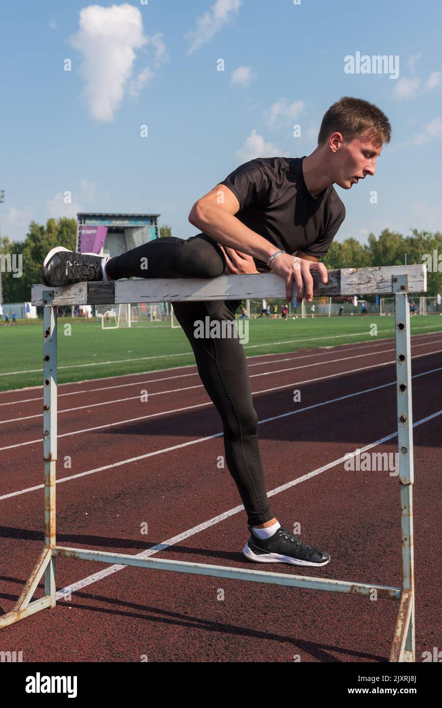 Junger sportlicher Mann Athlet Läufer in Sportbekleidung Stretching vor Hürden im Stadion laufen Stockfoto