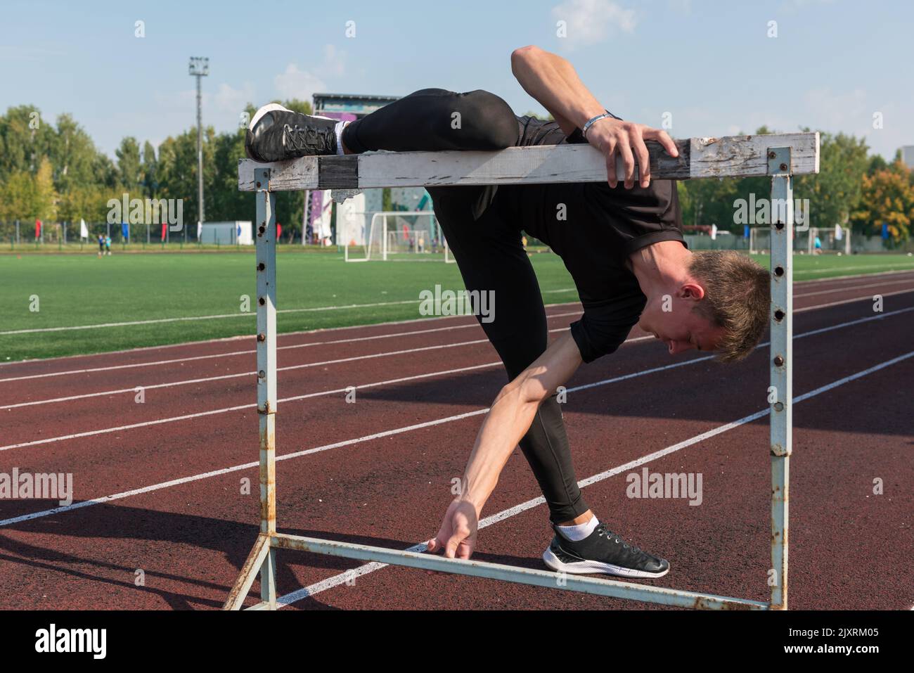 Junger sportlicher Mann Athlet Läufer in Sportbekleidung Stretching vor Hürden im Stadion laufen Stockfoto