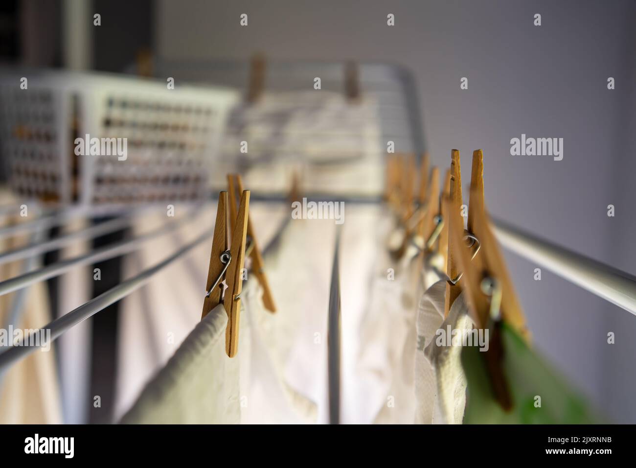 Gewaschene Kleidung, die mit Wäscheklammern an einer zusammenklappbaren Wäscheleine in einem Haus neben der Wärme eines Fensters hängt. Stockfoto
