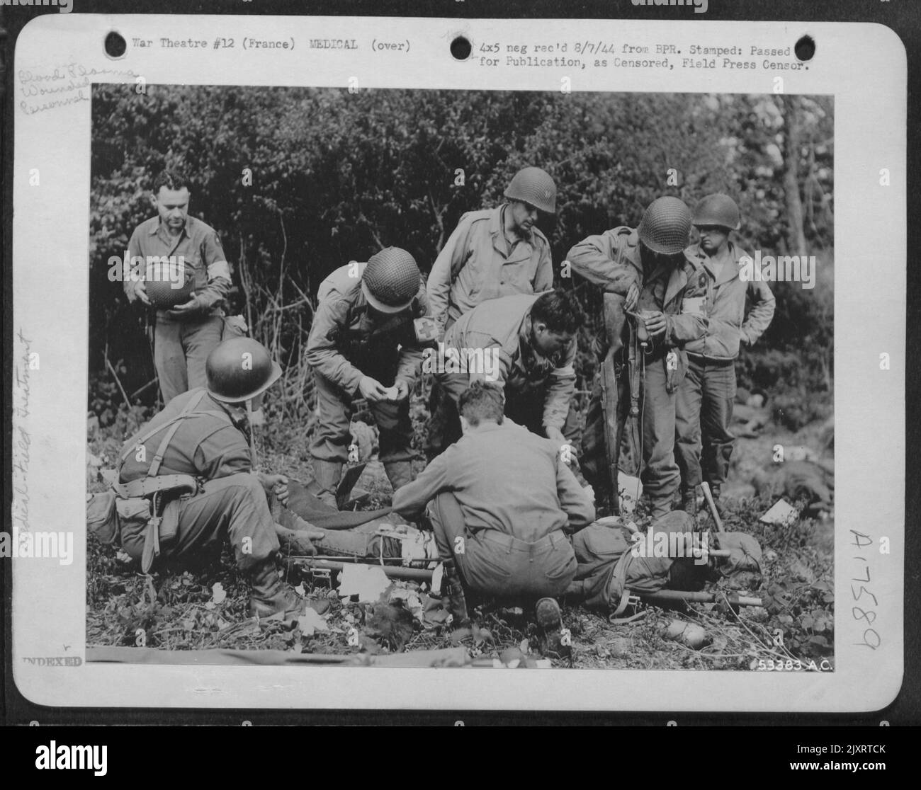 Blutplasma strömt aus der Flasche, die an das Gewehr eines verwundeten Soldaten gebunden ist, dessen Bein vorübergehend in eine Schiene gelegt wurde. Major Donald R. Roberts (der sich über den Patienten beugte, ohne Hut) leitet zu den Operationen, die von anderen Sanitätern an vorderster Front unterstützt werden. Stockfoto