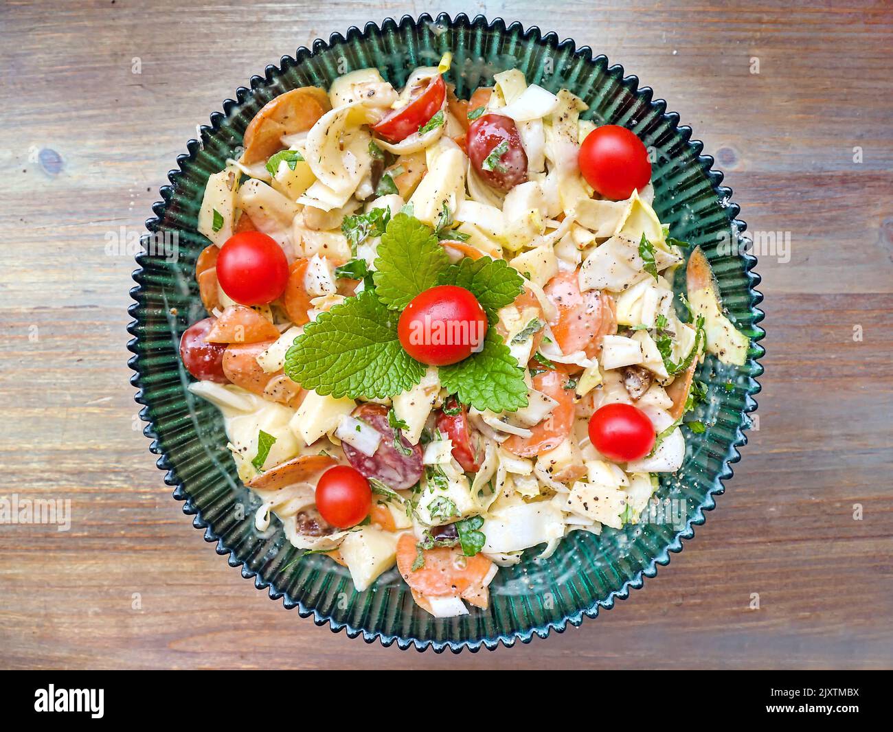 Salat aus Chicorée-Stücken mit Äpfeln, Kirschtomaten und in Scheiben geschnittenen Karotten, garniert mit Zitronenmelisse und Tomaten. Draufsicht, dunkelgrüne Glasplatte mit Stockfoto