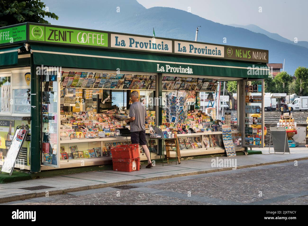 Mann, der ein Papier in einem kleinen Kiosk/Geschäft kauft, in dem Getränke, Zeitungen und Zeitschriften verkauft werden, Gravedona, Italien. Stockfoto