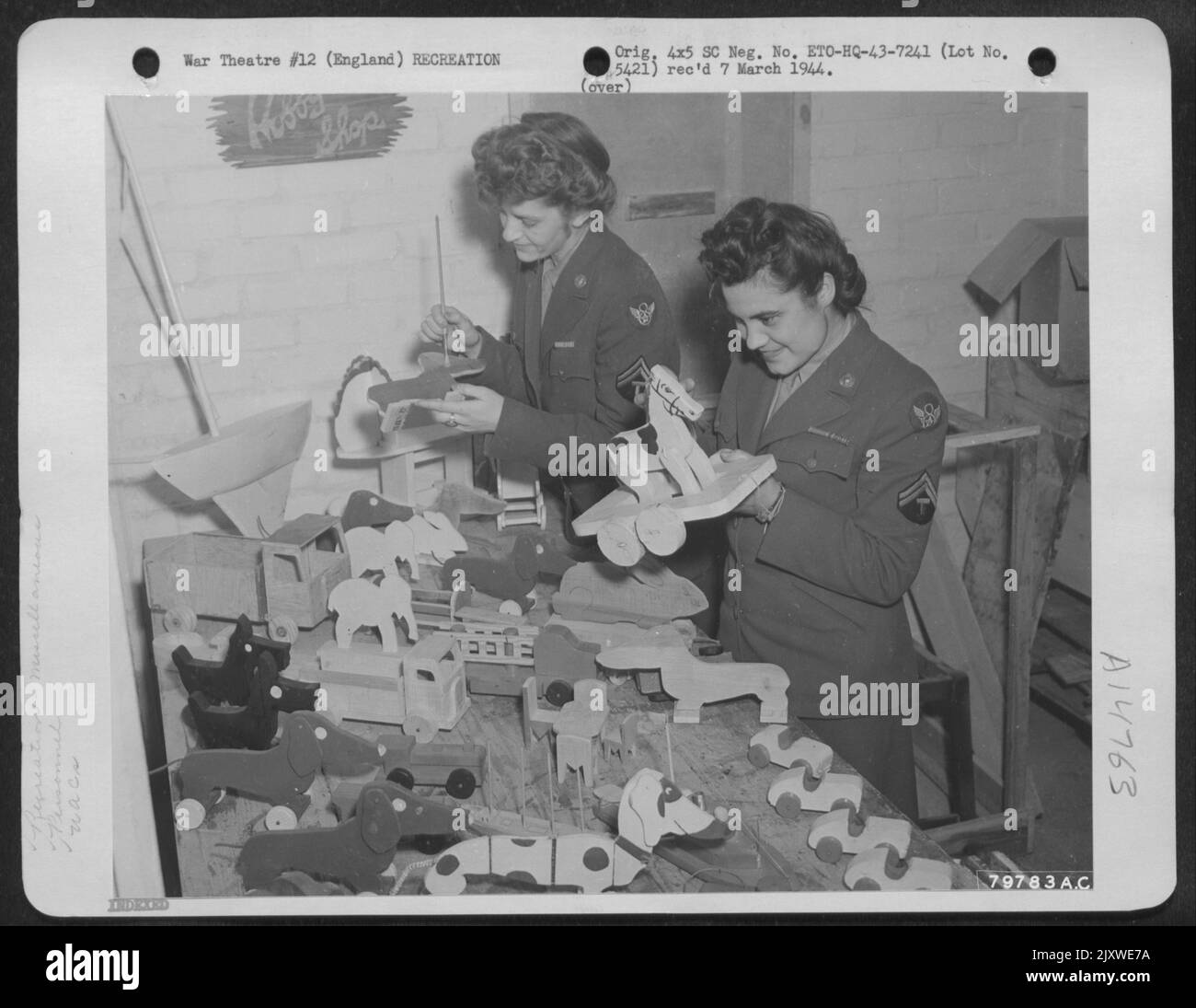 T/5 Louise Wesemann aus Lagrange, Illinois, und T/5 Mary Wahl aus Fairfax, Minnesota, WAC Stenografen, die auf einem Flugplatz in Middlesex, England, stationiert sind, geben großzügig von ihrer Spare Time to Paint Toys made by 8. Air Force Unit zur Verteilung auf Englisch oder Stockfoto