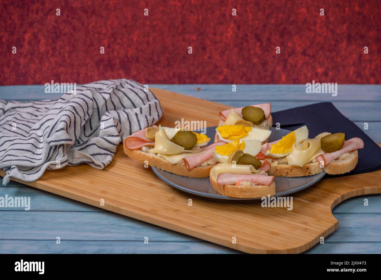 Typisches tschechisches offenes Sandwich mit Eiern, Kartoffelsalat, Schinken, Käse und Gurken auf einem blauen Holztisch Stockfoto