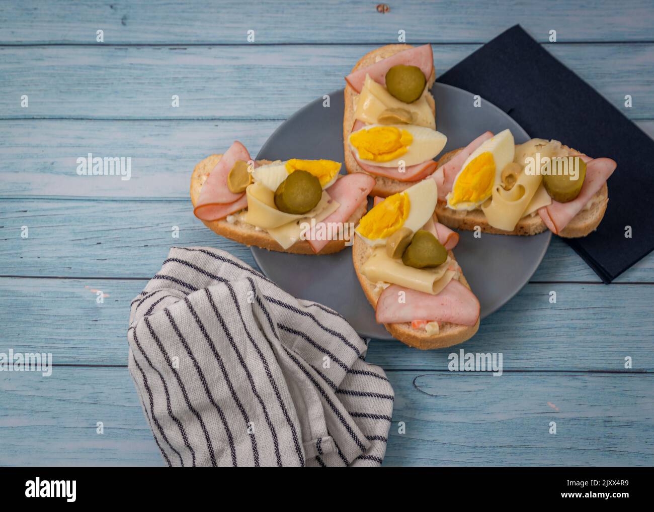Typisches tschechisches offenes Sandwich mit Eiern, Kartoffelsalat, Schinken, Käse und Gurken auf einem blauen Holztisch Stockfoto